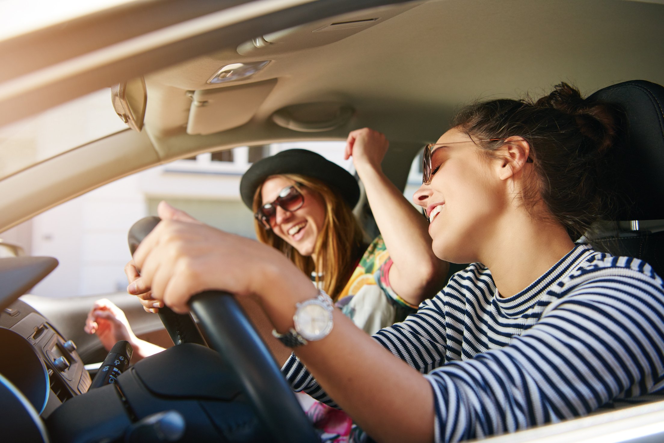 Friends singing joyfully in a car as they cruise along the scenic streets of Perth, Australia, with smiles on their faces, enjoying the moment.