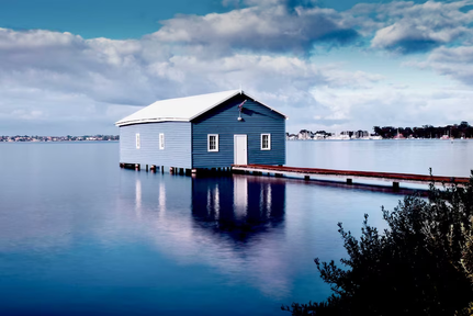 a blue house sits on a dock in the middle of swan river , perth, australia