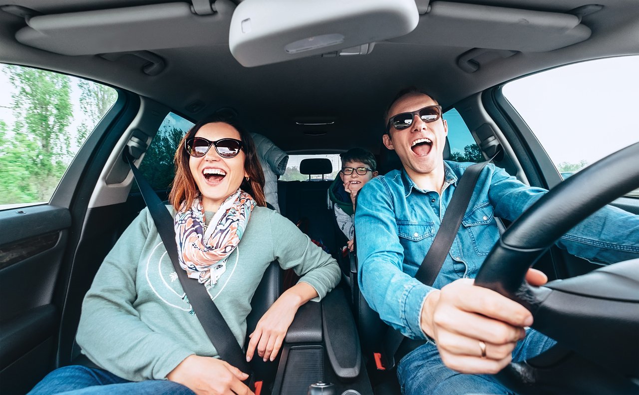  A joyful family of four singing together in their car while driving, with smiles on their faces and a karaoke machine in the car's dashboard. The parents are in the front seats, while the children are in the back, and having fun in tesla karaoke